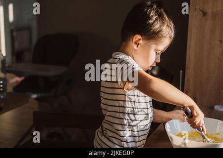 Kaukasischer Junge, der Zutaten für einen Kuchen in einer Schüssel in der Küche mischt. Kid Mischen sieben Mehl Pulver in Schüssel, Mischen und schlagen Teig mit Whist. Stockfoto