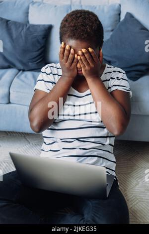 afroamerikanische Geschäftsfrau, die mit einem Laptop auf dem Boden sitzt, gestresst mit der Hand auf dem Gesicht, wütend und frustriert. afroamerikanische Frau Stockfoto