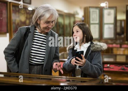 Präteen Mädchen mit Großmutter, die Telefon, um Informationen über Exponate im Museum zu finden Stockfoto