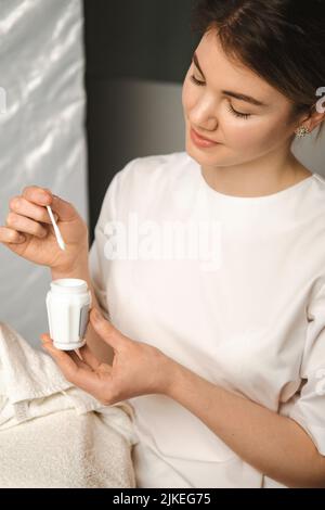 Hände einer Kosmetikerin, die im Spa-Salon ein Glas mit Maske und Spachtel hält. Hände einer Ärztin, die eine Flasche Creme hält. Konzentrieren Sie sich auf die Hände mit Stockfoto