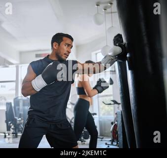 Aktiver, fitger und ernsthafter Mann beim Boxen, beim Schwitzen und beim Cardio-Training im Fitnessstudio. Ein sportlicher, schweißtreibender und entschlossener Athlet, der müde aussieht Stockfoto