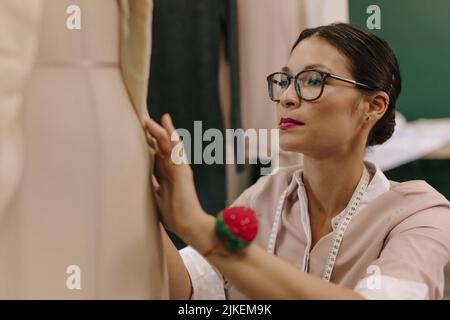 Asiatische Mode-Designer Fixierung Kleid auf Schaufensterpuppe in ihrem Studio. Weibliche Schneiderin arbeitet an Designer-Kleid auf Schaufensterpuppe. Stockfoto
