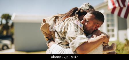Eine Soldatin umarmte ihren Mann, nachdem sie von der Armee nach Hause zurückgekehrt war. Amerikanische Militärangehörende, die nach Serv ein emotionales Wiedersehen mit ihrem Mann hatte Stockfoto