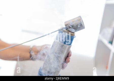 Selektiver Fokus einer Hand mit Behälter mit Stickstoff, der in eine Kryotherapiepistole platziert wird Stockfoto