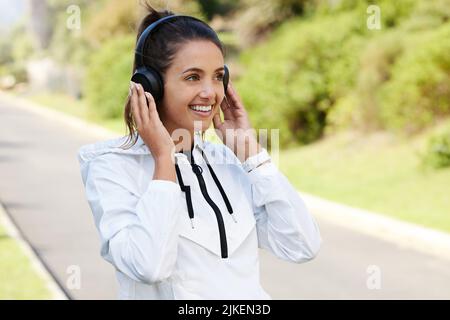 Dieser Song bringt mich in Laufstimmung. Eine attraktive und athletische junge Frau, die im Freien Musik hört. Stockfoto
