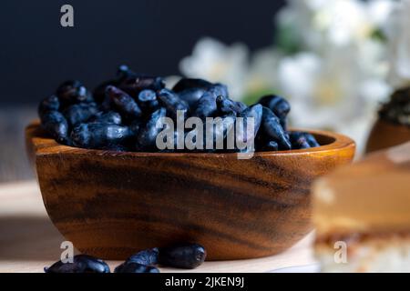 Geißelbeeren in einem Holzteller, reife gesunde Geißelbeeren auf dem Küchentisch Stockfoto