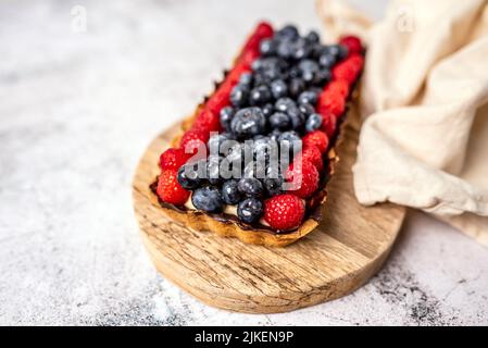 Obsttarte voller Beeren mit Schokolade und Rahm auf Kekskruste. Europäische Dissertation. Stockfoto