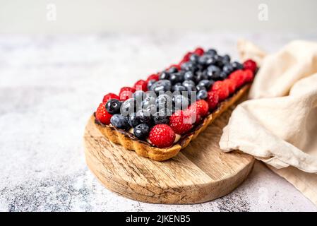 Obsttarte voller Beeren mit Schokolade und Rahm auf Kekskruste. Europäische Dissertation. Stockfoto