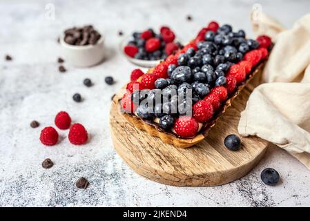 Obsttarte voller Beeren mit Schokolade und Rahm auf Kekskruste. Europäische Dissertation. Stockfoto