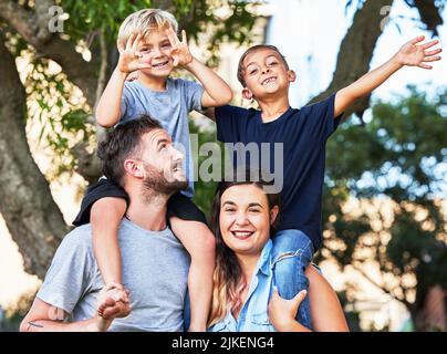 Lobt eure Kinder offen, rühmt sie heimlich. Porträt einer schönen Familie mit ihren Söhnen auf den Schultern in einem Park. Stockfoto