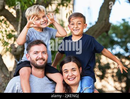 Vater – jemand, der Bilder trägt, wo er einst Geld aufbewahrt hat. Porträt einer schönen Familie mit ihren Söhnen auf den Schultern in einem Park. Stockfoto