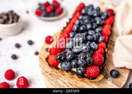 Obsttarte voller Beeren mit Schokolade und Rahm auf Kekskruste. Europäische Dissertation. Stockfoto