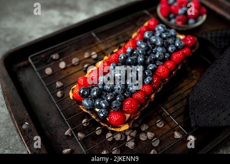 Obsttarte voller Beeren mit Schokolade und Rahm auf Kekskruste. Europäische Dissertation. Stockfoto