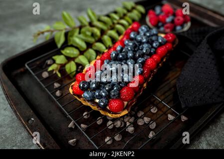 Obsttarte voller Beeren mit Schokolade und Rahm auf Kekskruste. Europäische Dissertation. Stockfoto