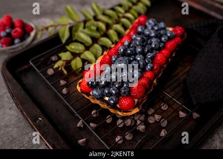 Obsttarte voller Beeren mit Schokolade und Rahm auf Kekskruste. Europäische Dissertation. Stockfoto