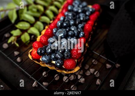 Obsttarte voller Beeren mit Schokolade und Rahm auf Kekskruste. Europäische Dissertation. Stockfoto