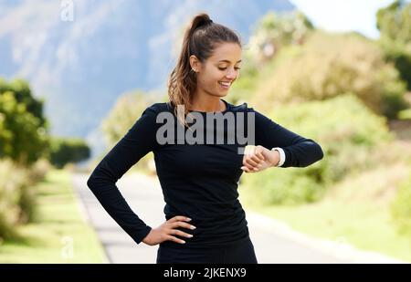 Das ist eine tolle Zeit. Eine attraktive und athletische junge Frau, die ihre Uhr überprüft, während sie im Freien steht. Stockfoto