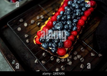 Obsttarte voller Beeren mit Schokolade und Rahm auf Kekskruste. Europäische Dissertation. Stockfoto