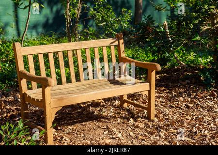 Eine leere Holzbank in einem Park mit trockenen Blättern. Stockfoto