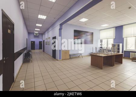 Schulflur, Flur der Hochschule oder Universität. Hellblaue Wände, braune Türen und gefliester Fußboden. Stockfoto