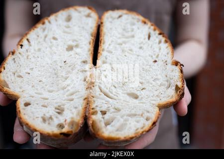 Der Bäcker zeigt einen Schnitt des fertigen handwerklichen Brotes. Der Prozess der Brotherstellung in der handwerklichen Bäckerei. Vorderansicht. Stockfoto