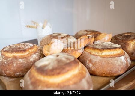 Handwerkliches Brot nur aus dem Ofen auf dem Tisch in einer kleinen Hausbäckerei. Vorderansicht. Stockfoto