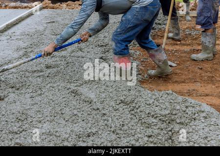 Baustellenmitarbeiter gießen feuchten Beton, während eine Auffahrt gepflastert wird Stockfoto