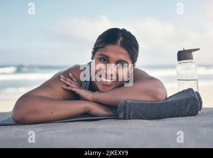 Nach dem Workout fühle ich mich super entspannt. Eine sportliche junge Frau, die auf ihrer Yogamatte am Strand liegt. Stockfoto