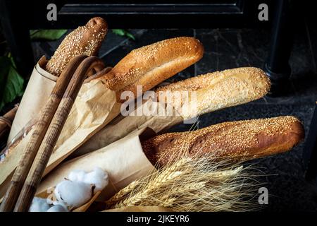 Frisch gebackenes Brot liegt in einem Korbkorb. Mehrere verschiedene frische Brote in Öko-Paket zusammen mit Ähren von Weizen. Stockfoto