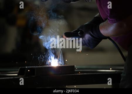 Der Handwerker, der an seinem Arbeitsplatz in der Werkstatt Schweißen und Schleifen durchführt, während die Funken um ihn herum „fliegen“. Er trägt einen Schutzhelm und Stockfoto