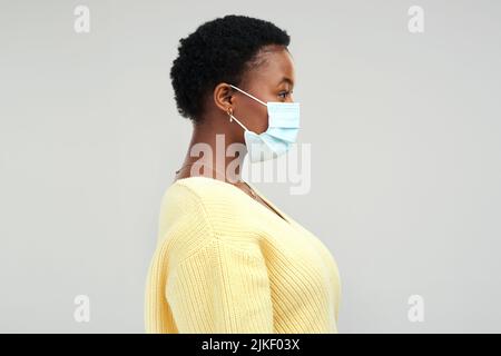 Bitte tragen Sie Ihre Maske. Eine junge Frau trägt eine OP-Maske, während sie vor einem grauen Hintergrund steht. Stockfoto