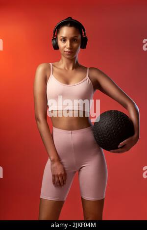 Seht zu, wie ich es Töte, wie ich es immer tue. Studioportrait einer sportlichen jungen Frau, die einen Übungsball vor einem roten Hintergrund hält. Stockfoto