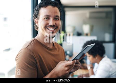 Mein Tablet macht mich so glücklich. Ein junger Geschäftsmann, der ein digitales Tablet im Büro benutzt. Stockfoto