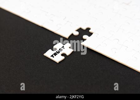 VERTRAUEN Sie Text auf weißem Puzzle mit fehlenden Stück auf schwarzem Hintergrund. Business Trust Partnerschaft und Teamwork-Konzept. Vertrauen und Beziehung. Stockfoto