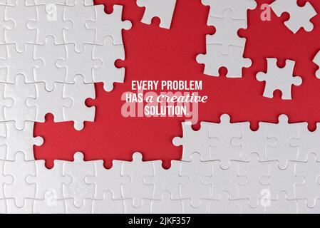 Lebensinspirierendes und motivierendes Zitat - jedes Problem hat eine kreative Lösung. Mit weißem Puzzle und einigen fehlenden Teilen auf rotem Hintergrund. Stockfoto