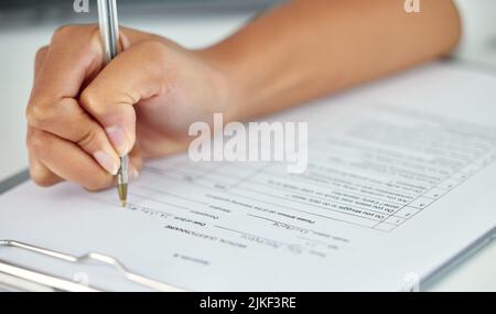Eine nicht erkennbare Geschäftsfrau, die einen Fragebogen ausfüllt, während sie in ihrem Büro sitzt. Stockfoto