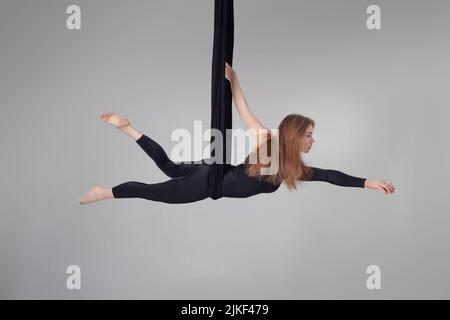 Schönes Mädchen in einem schwarzen Sportanzug führt eine akrobatische Elemente in einem Studio. Stockfoto