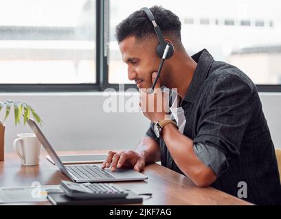 Lassen Sie mich darüber nachdenken: Ein hübscher junger, männlicher Call Center-Agent, der bei der Arbeit an seinem Laptop nachdenklich aussieht. Stockfoto
