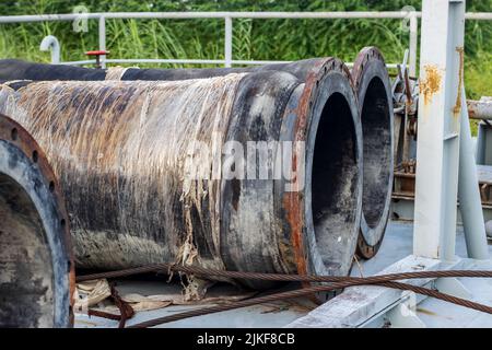 Rustikale verlassene Baggerrohre, die auf einem Schiff in der Nähe des Waldes gelagert wurden, sind aus nächster Nähe zu sehen Stockfoto