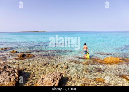 Junge, der an einem Strand mit Schnorchelflossen in den Händen an einem wunderschönen Veli ZAL Strand, Dugi otok, Kroatien, steht Stockfoto
