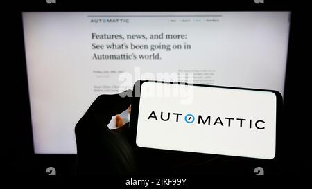 Person, die Mobiltelefon mit dem Logo des US-Distributed Company Automattic Inc. Auf dem Bildschirm vor der Business-Webseite hält. Konzentrieren Sie sich auf die Telefonanzeige. Stockfoto