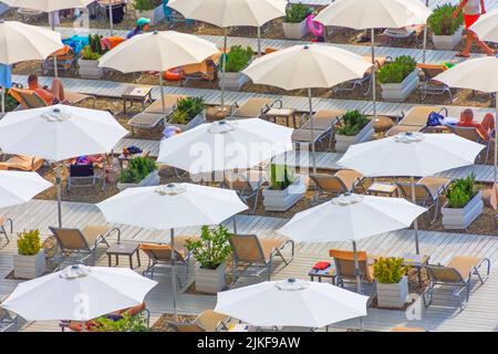 Sonnenschirme und Liegestühle mit Spazierwegen und Blumentöpfen mit Pflanzen am Strand Stockfoto