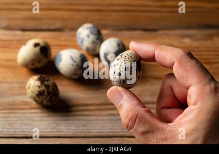 Männliche Hand hält ein Wachtelei auf einem hölzernen Hintergrund. Nahaufnahme. Stockfoto