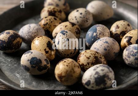 Wachteleier in einer eisernen Schüssel vor einem hölzernen Hintergrund platziert. Stockfoto