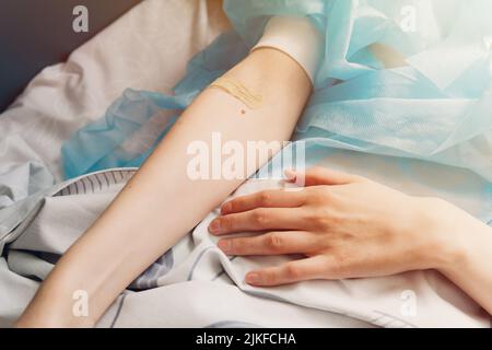 Nahaufnahme einer weiblichen Hand mit einem Pfand am Arm. Patient liegt nach der Operation auf einem Krankenhausbett. Stockfoto