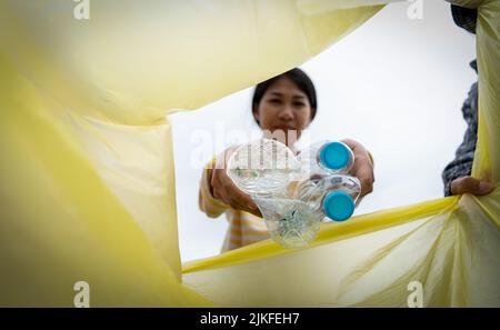 Frau wirft Plastikmüll in einen Müll. Frau, die Müllplastiktüten in den Müll legt Stockfoto