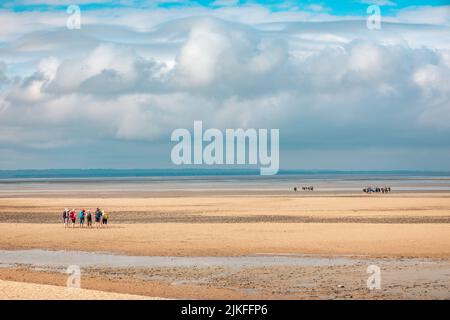 Gruppen von Touristen, die den Ärmelkanal von der Plage du Bec d'Andaine zu Fuß überqueren, um den Mount Saint-Michel zu erreichen Stockfoto