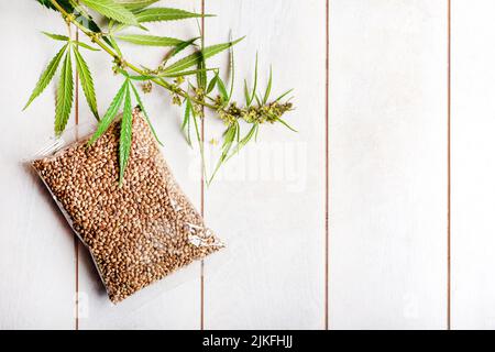 Transparente Tasche mit Cannabissamen und einem Zweig frischen Cannabis auf einem hellen Holzhintergrund, Mockup Stockfoto