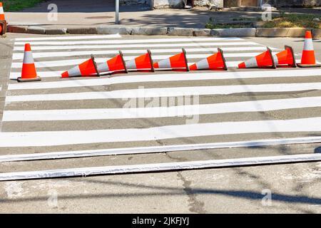 Frisch markierter Fußgängerüberweg mit orangefarbenen Verkehrskegeln an einem sonnigen Sommertag. Speicherplatz kopieren. Stockfoto