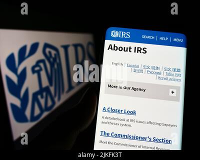 Person, die Mobiltelefon mit der Webseite des US Internal Revenue Service (IRS) auf dem Bildschirm vor dem Logo hält. Konzentrieren Sie sich auf die Mitte des Telefondisplays. Stockfoto